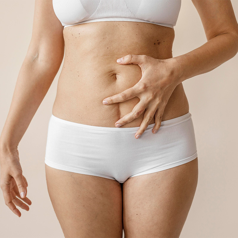 Mujer en ropa interior blanca señalando la zona central de su abdomen.